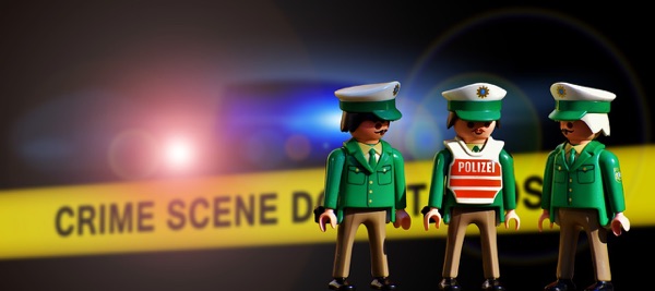 Three toy police figures standing behind yellow crime scene tape