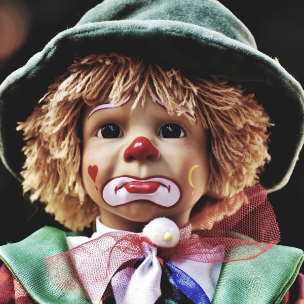 A sad-faced clown doll with a green hat and yarn hair